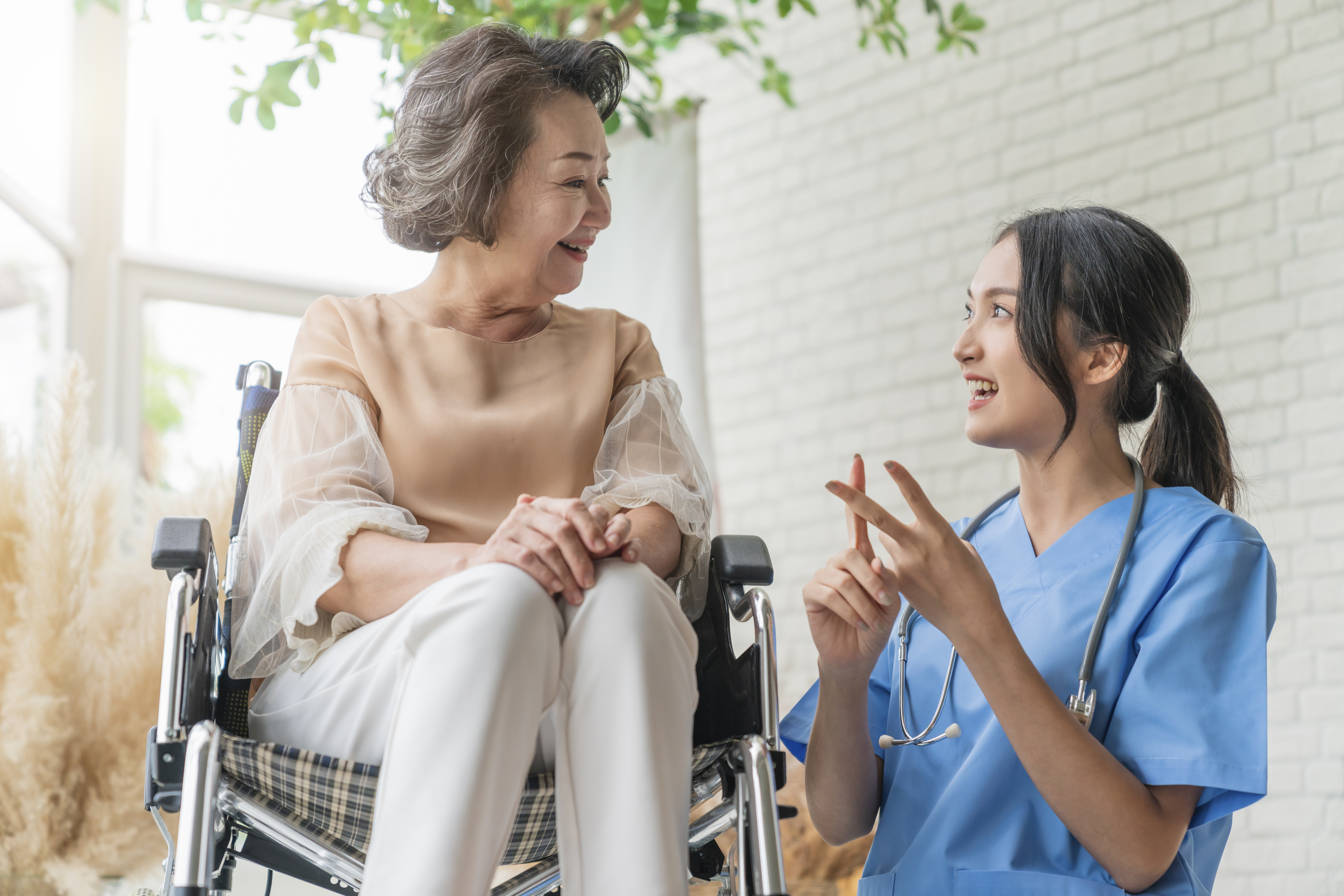 asian young caregiver caring for her elderly patient at senior daycare Handicap patient in a wheelchair at the hospital talking to a friendly nurse and looking cheerful nurse wheeling Senior patient